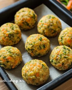 Bolitas de verduras con zanahoria, brócoli y calabacita, listas para hornear en una bandeja negra con papel encerado.