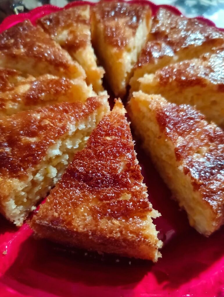 Pan de elote sin harina, cortado en porciones triangulares sobre un plato rojo, con superficie dorada y textura húmeda.