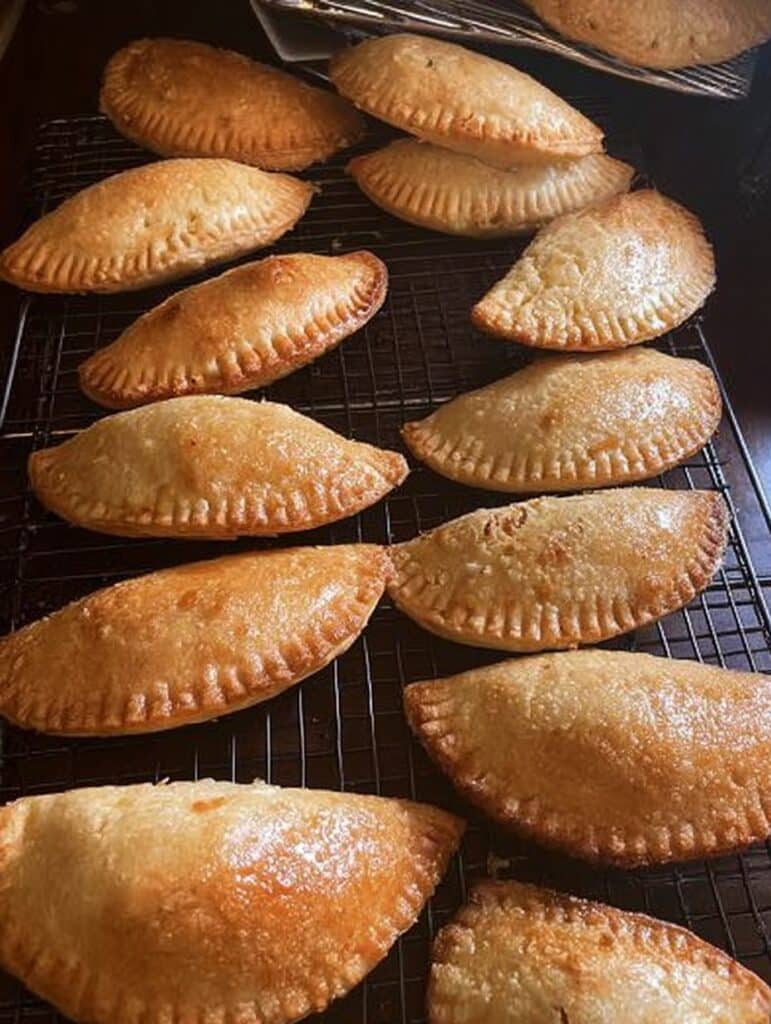 Empanaditas de cajeta doraditas recién horneadas sobre una rejilla enfriadora.