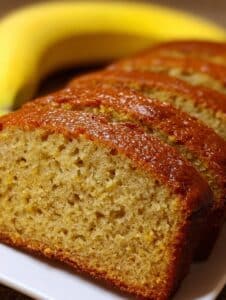 Pan de banana sin harina, esponjoso y húmedo, acompañado de una banana madura en el fondo.