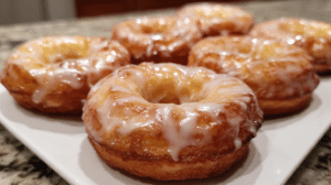 Fluffy cottage cheese protein donuts with vanilla glaze on a white plate, showing golden-brown baked texture and glossy sweet glaze dripping down sides