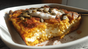 Golden pumpkin cottage cheese breakfast bake in white ceramic baking dish, cut into squares showing fluffy texture, garnished with cinnamon and served on rustic wooden table