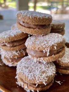 Alfajores integral rellenos de dulce de leche sin azúcar y cubiertos con coco rallado, servidos en un plato de cerámica.