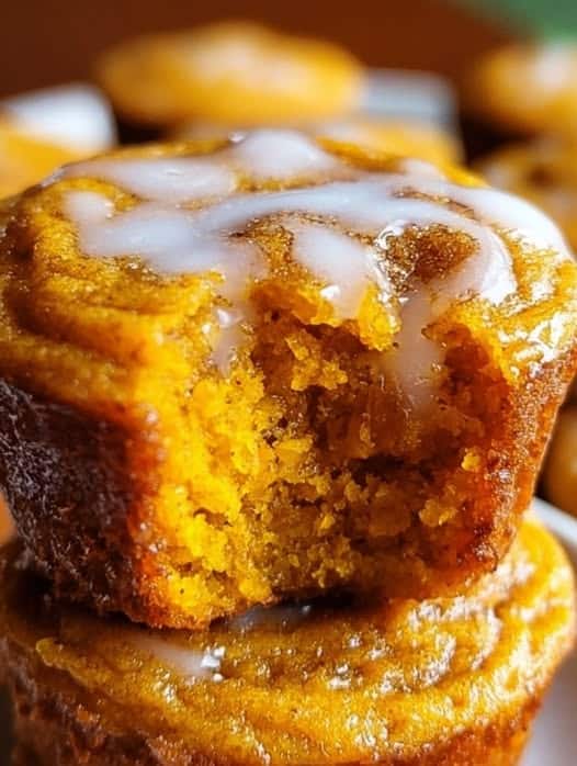 Close-up of moist flourless pumpkin muffin with a bite taken out and a drizzle of icing on top.