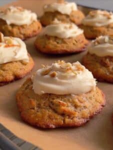 Galletas de tarta de zanahoria con frosting cremoso y nueces encima, sobre bandeja de horno.