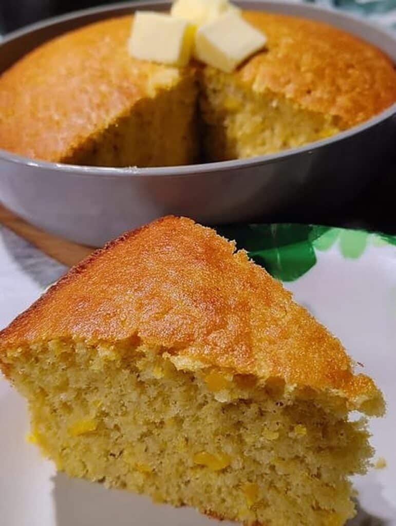 Pan de elote en licuadora recién horneado, esponjoso y dorado, servido en rebanada con trozos de mantequilla encima.