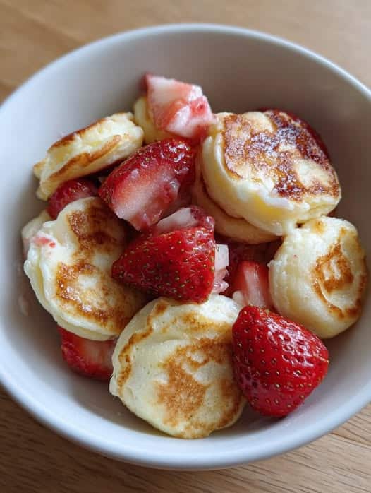 Bowl of strawberry vanilla cottage cheese pancake bites served with fresh strawberries