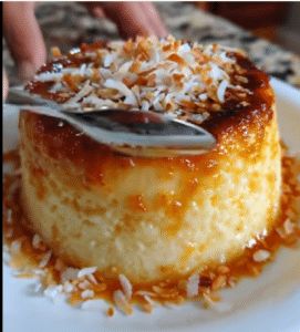 Flan de elote y queso cubierto con coco rallado y caramelo dorado sobre un plato blanco.