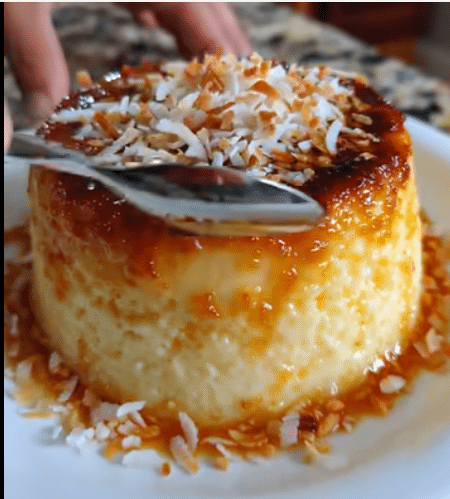 Flan de elote y queso cubierto con coco rallado y caramelo dorado sobre un plato blanco.