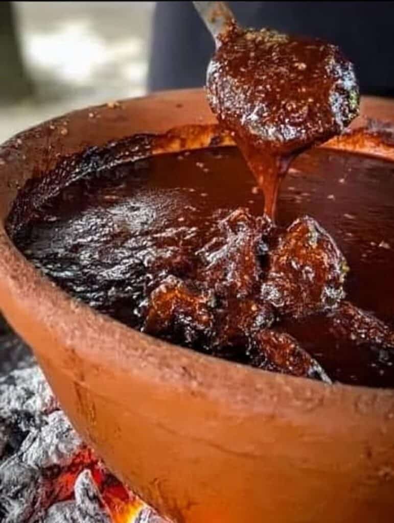 Mole casero cocinándose en olla de barro sobre brasas, con textura espesa y color intenso.